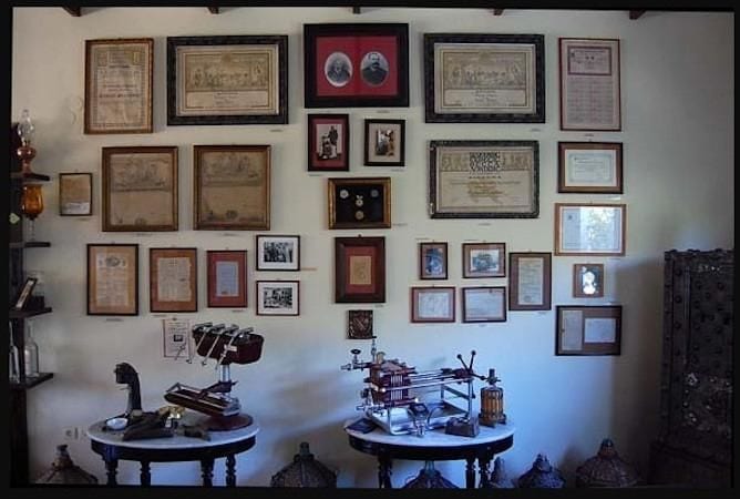wooden rotund tables in a room with antiquities and framed photos at Karonis Distillery museum
